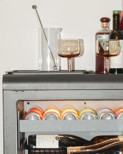 Two people gathered on either side of the Rocco fridge. The person on the left is smiling and holding a bottle of pink wine. 