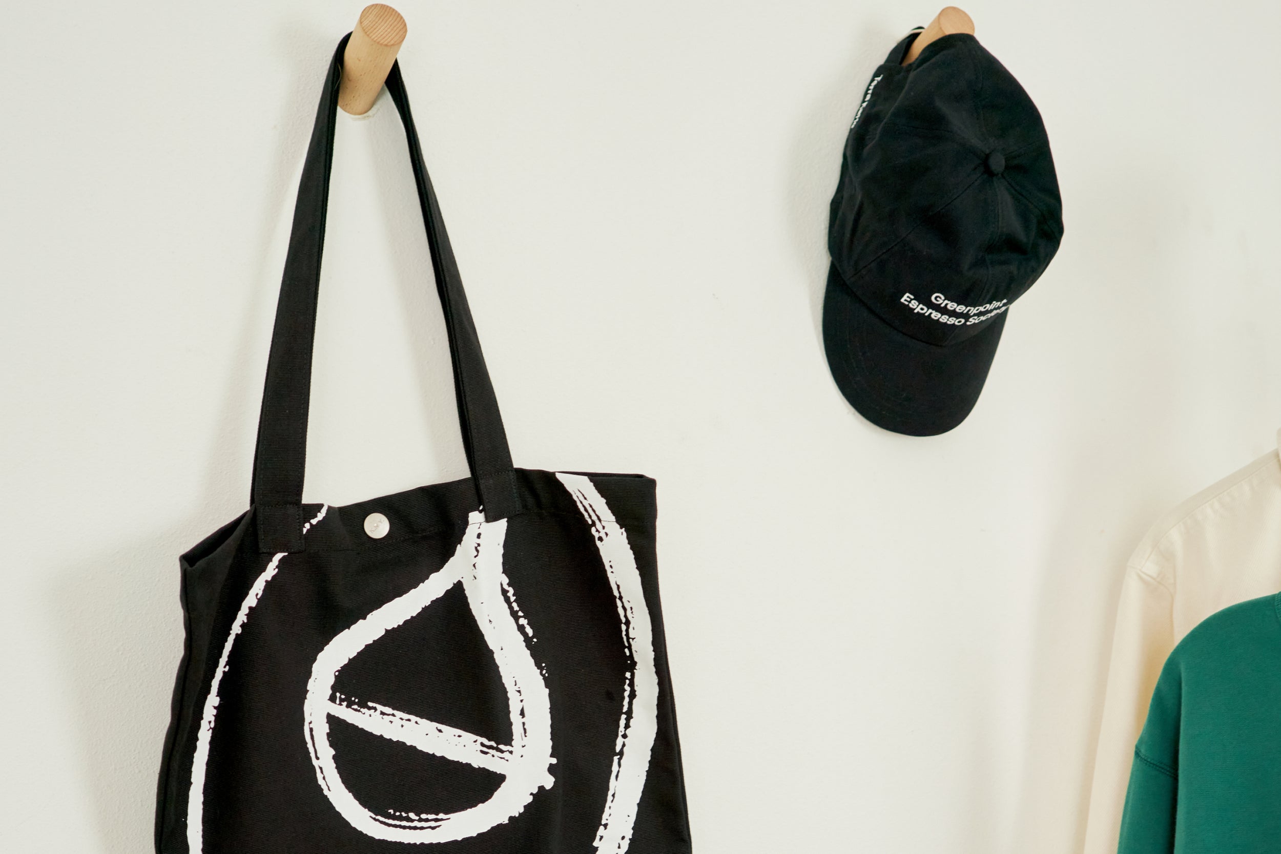 Terra Kaffe | Black tote bag, black baseball cap, and green sweater hanging on a wall