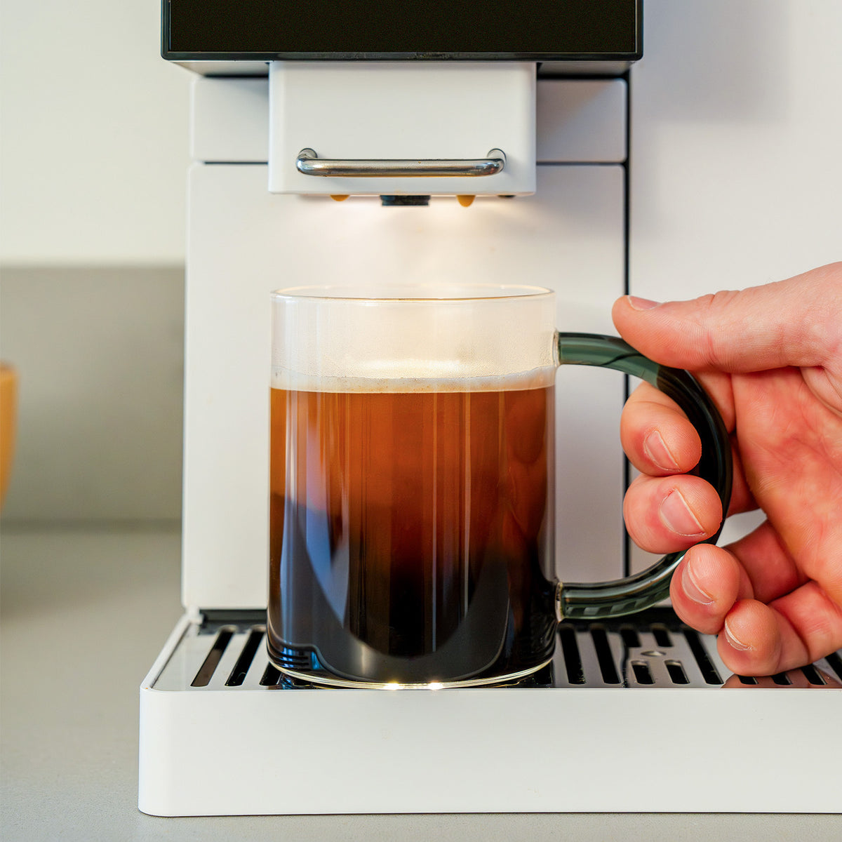 A hand reching for a cup with drip coffee that's standing under the spout of the TK-02